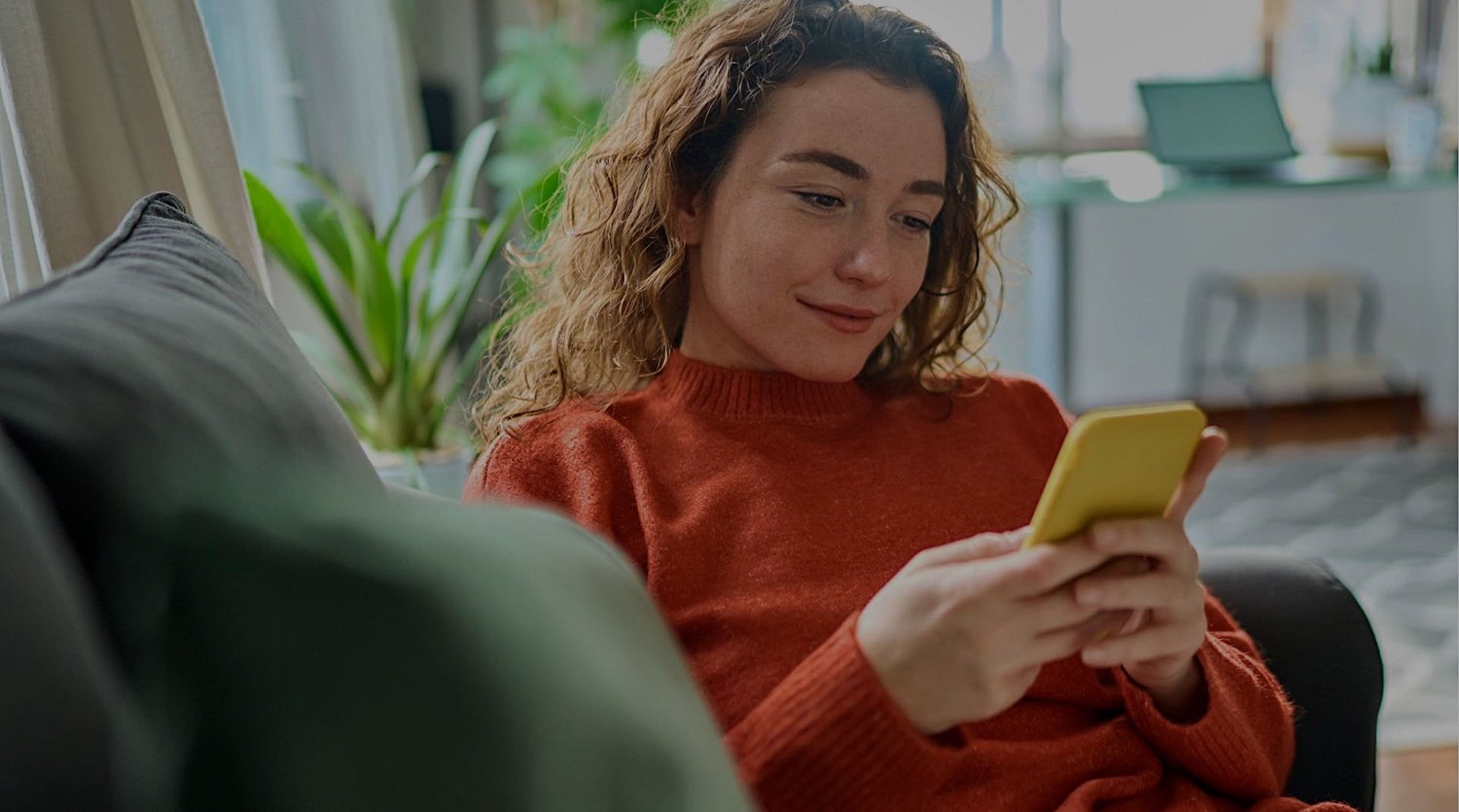 自宅のソファでリラックスしながら黄色いスマートフォンを見て微笑む女性。Walmartのショッピング体験を象徴する日常のワンシーン。